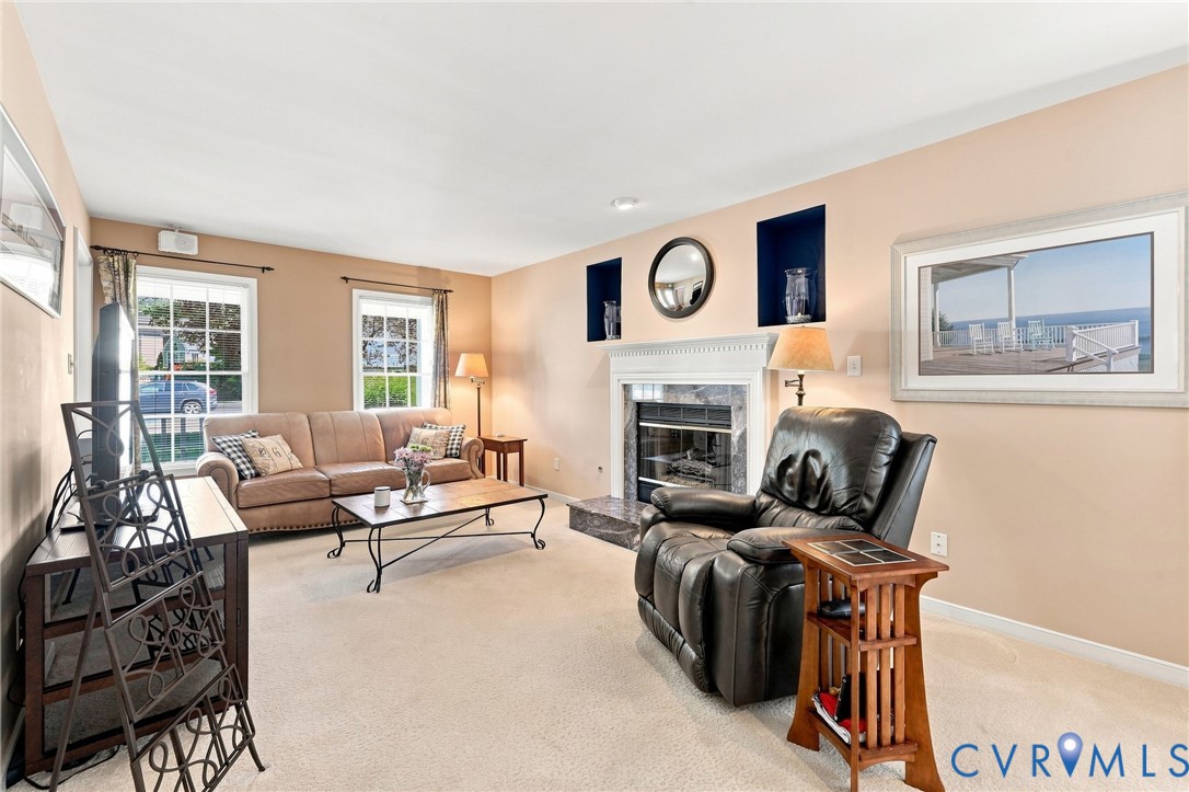 Carpeted living area featuring a fireplace with a stone surround, a white mantel, and two recessed wall niches