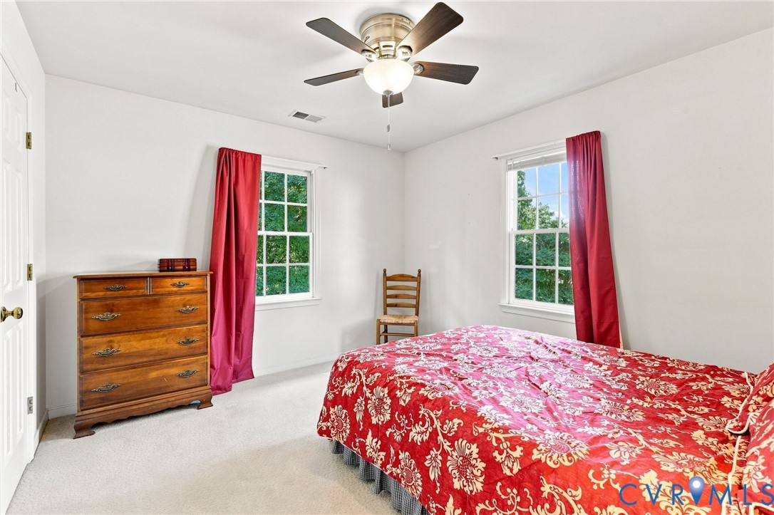 Bright interior with white walls, carpet flooring, a ceiling fan with integrated lighting, and two windows