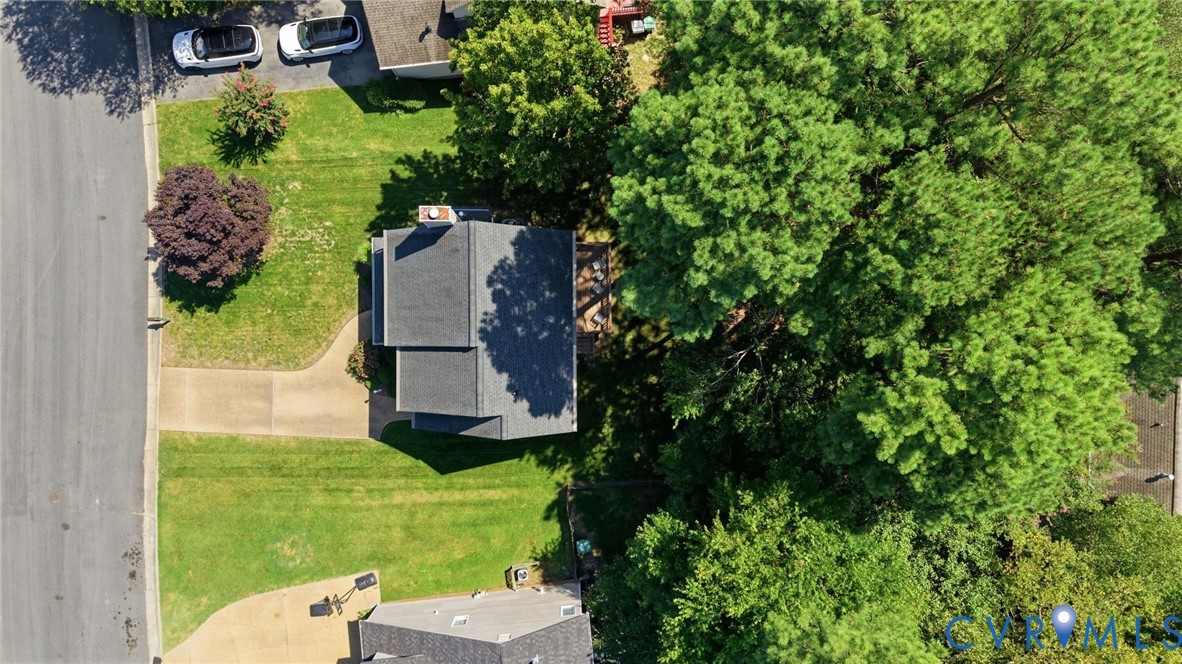 Paved driveway leading to a residence with a gray shingle roof, surrounded by mature trees and a green lawn