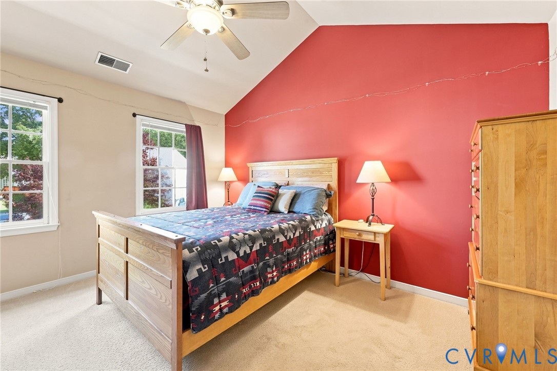 Vaulted ceiling with a ceiling fan, two double-hung windows, and light-toned carpeting