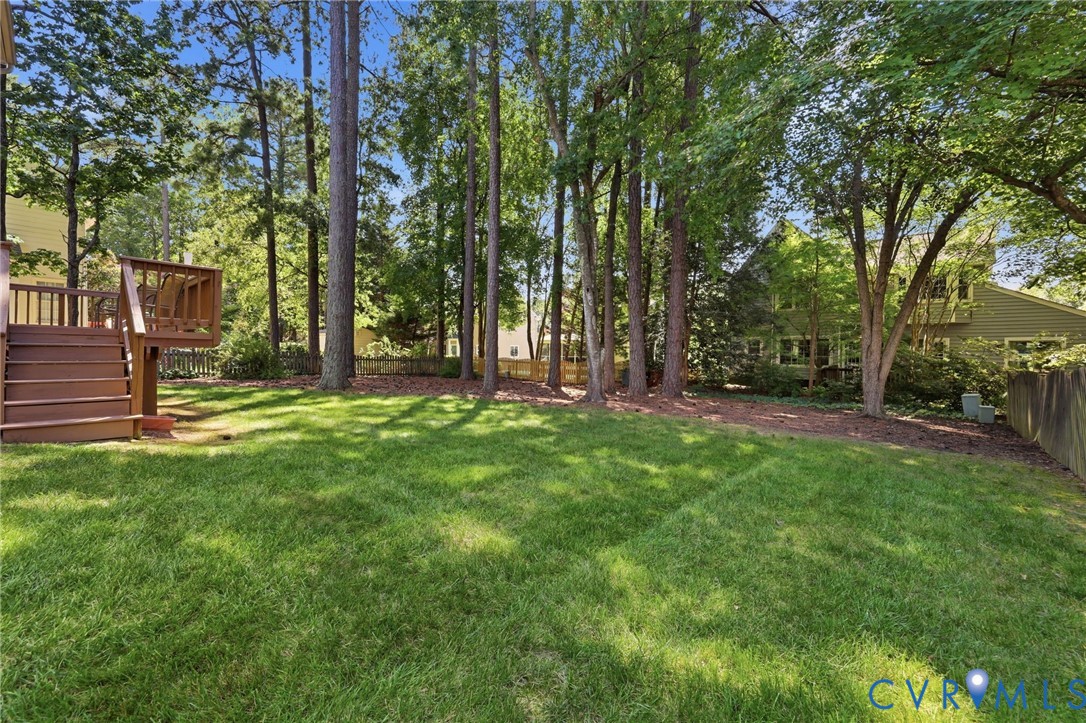 Expansive green lawn, multi-level wood deck, mature trees, and natural landscaping