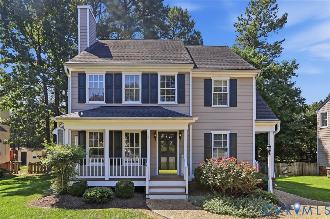 Two-story residence featuring light-colored siding, dark shutters, and a covered front porch with white railings