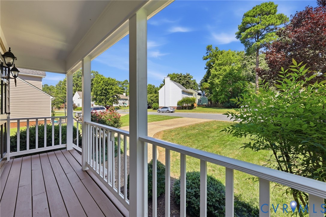 Covered front porch with wood-finish flooring, white railing, and exterior wall sconces