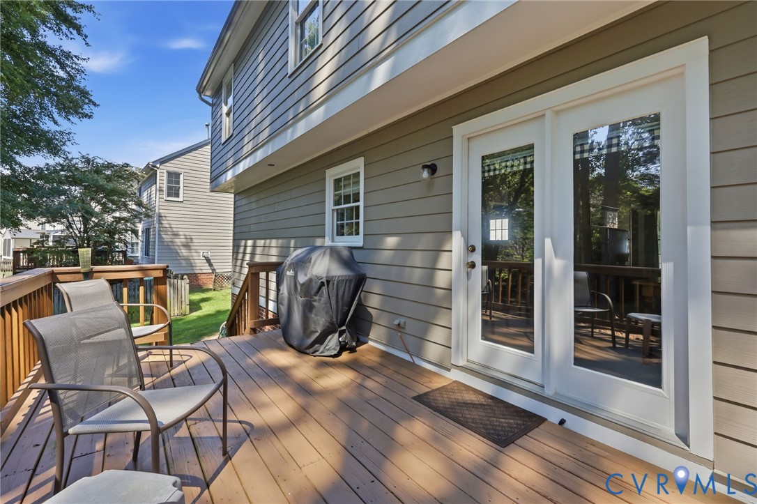 Expansive wood-finish deck with wood railings, featuring white-framed double doors and siding exterior