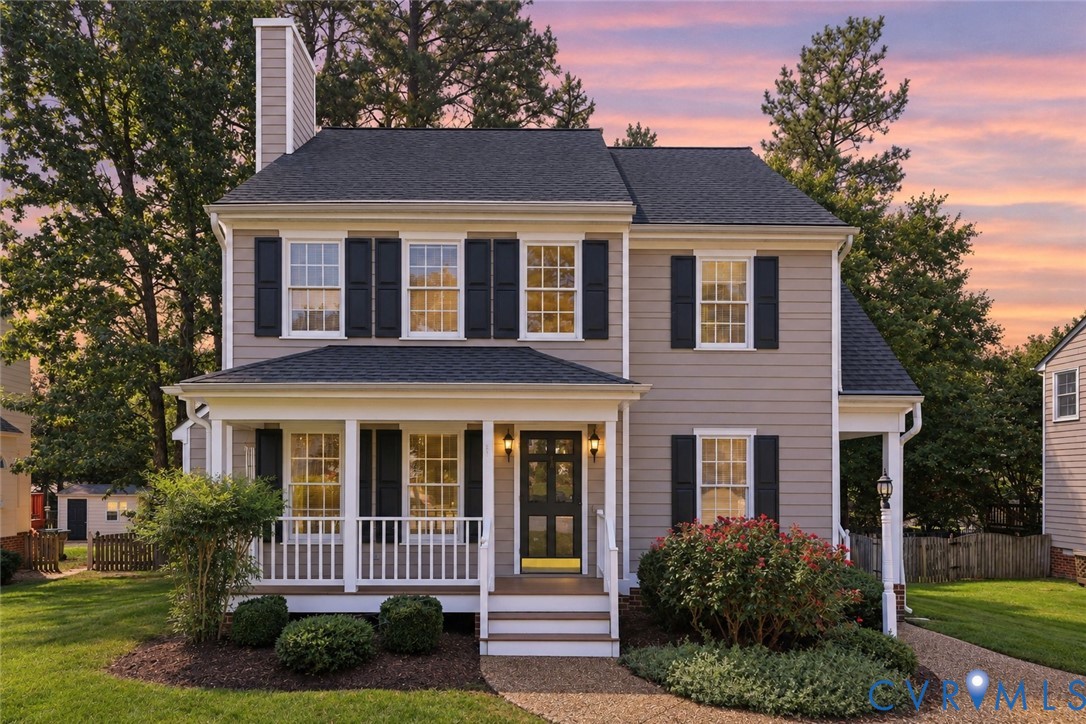 Two-story home with light-colored siding, contrasting dark shutters, and a covered front porch featuring white railings