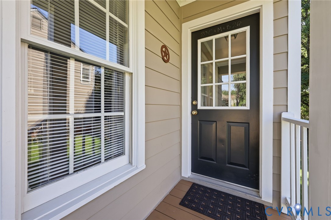 Black front door with a window pane insert, light-colored siding, and a white framed window