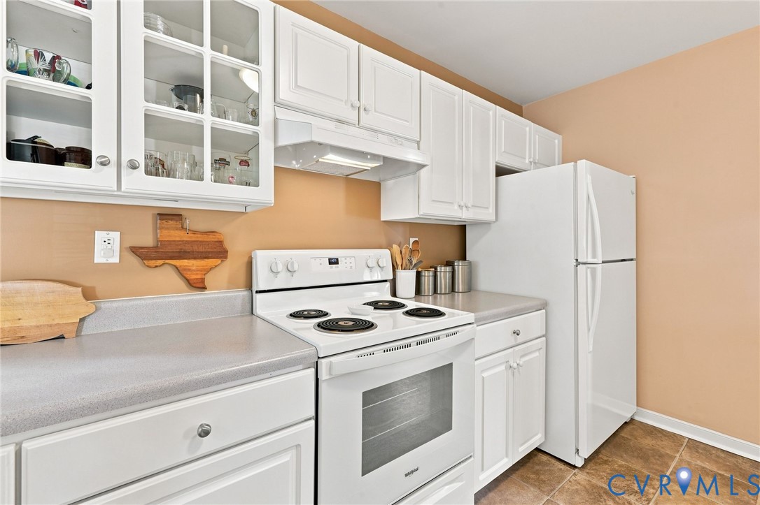 White cabinetry with glass-front upper cabinets, light gray countertops, white electric range, white refrigerator, and tile flooring