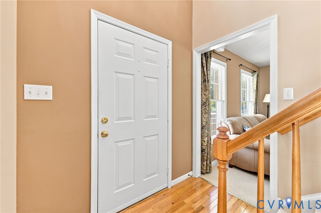 White paneled entry door with brass hardware, wood-finish flooring, and a natural wood staircase railing