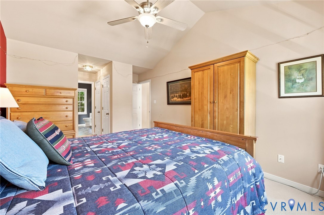 Vaulted ceiling with ceiling fan, light-toned wall paint, and carpeted flooring