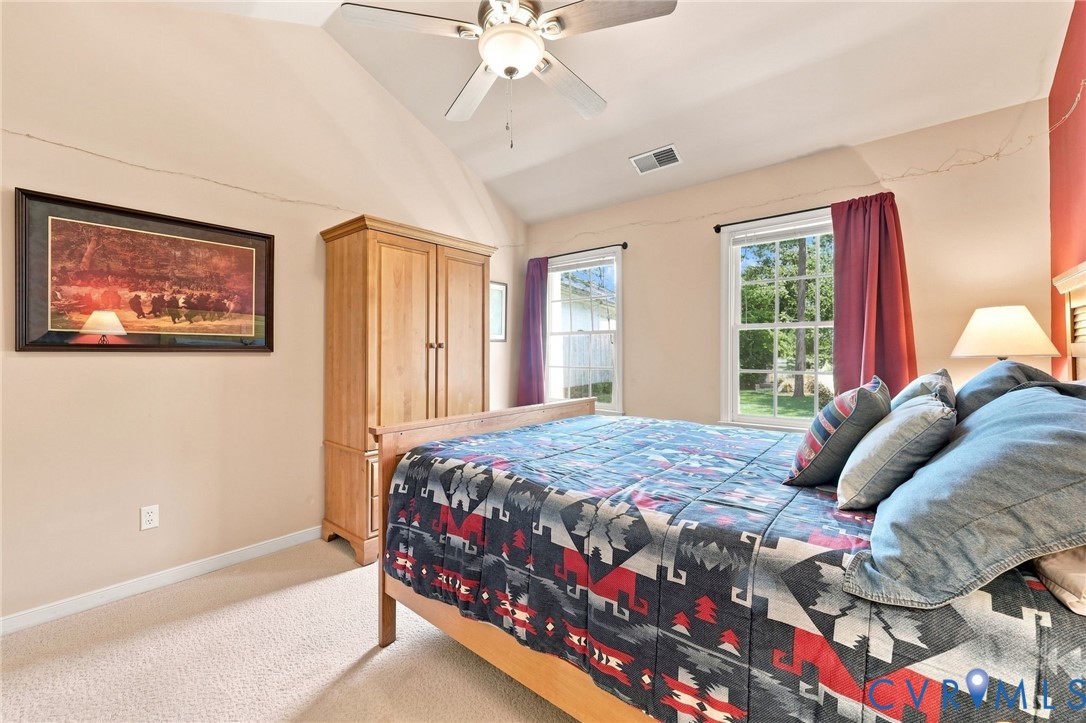 Vaulted ceiling, ceiling fan, two windows, wall-to-wall carpeting, and wood-finish door frame