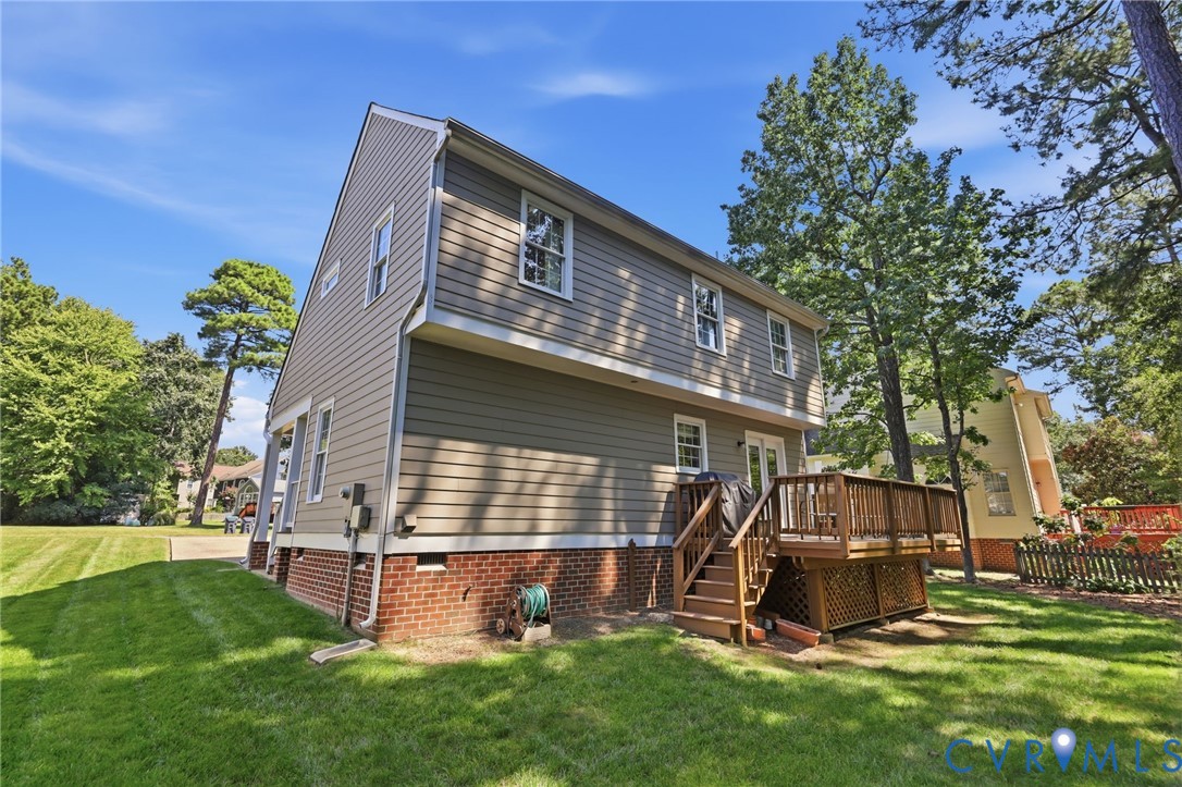 Brown siding exterior with a brick foundation, featuring a multi-level wood deck, white window trim, and a manicured lawn