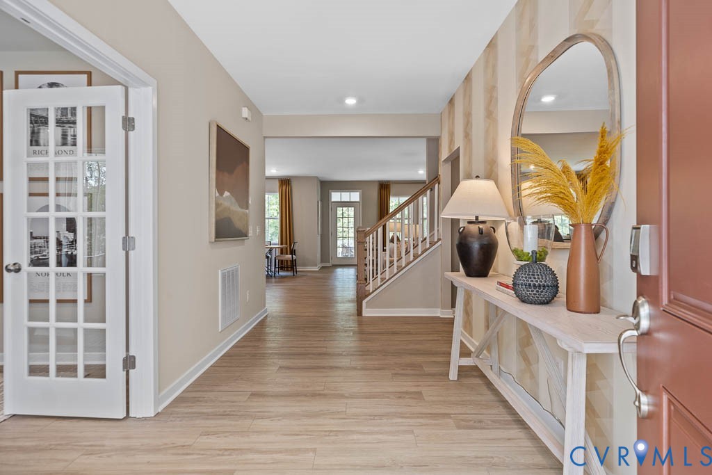 Inviting entryway featuring wood-finish flooring, a contemporary staircase with wood newel posts, and a French-door style room entrance