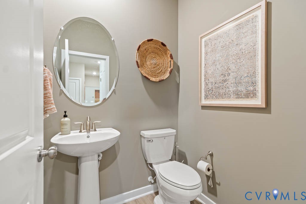 Pedestal sink with a brushed nickel faucet, oval frameless mirror, and wood-finish flooring