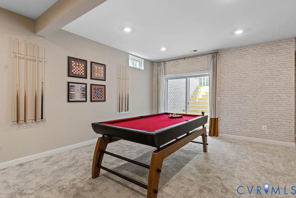 Recessed lighting, light gray carpeting, exposed brick wall, sliding glass door, and a built-in cue rack