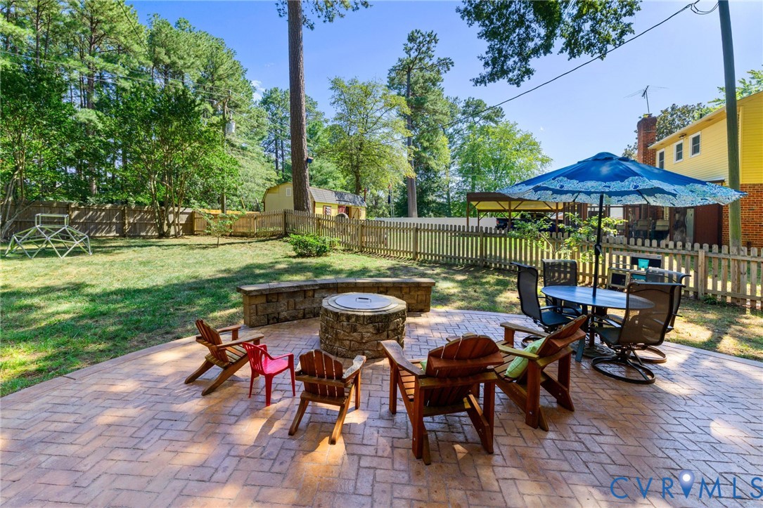 Expansive backyard featuring a stamped concrete patio, stone fire pit, and wood picket fencing