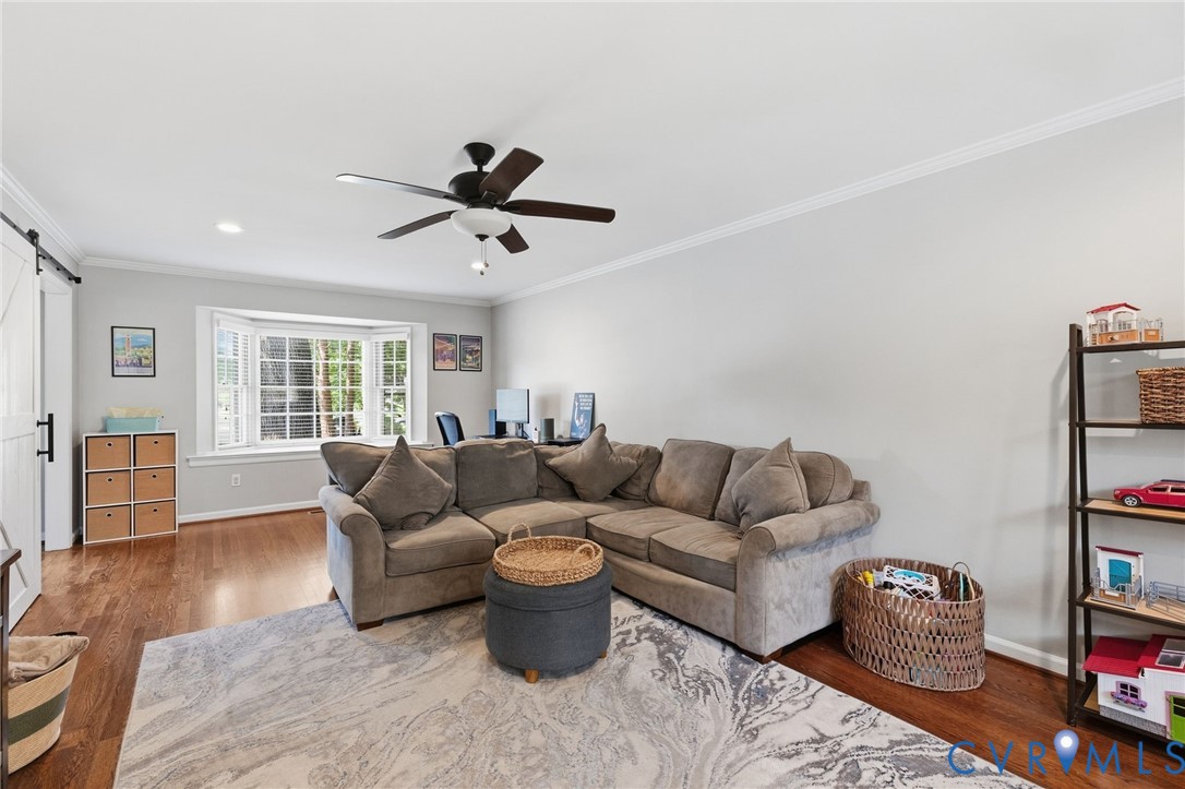 Hardwood flooring, bay window, white crown molding, recessed lighting, and a ceiling fan with light fixture