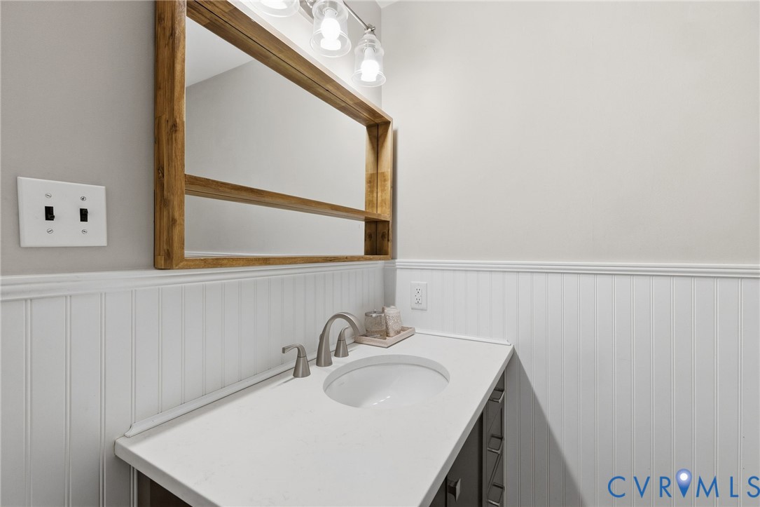 Beadboard wainscoting, integrated sink, wood-framed mirror, vanity with storage, and wall-mounted lighting fixture