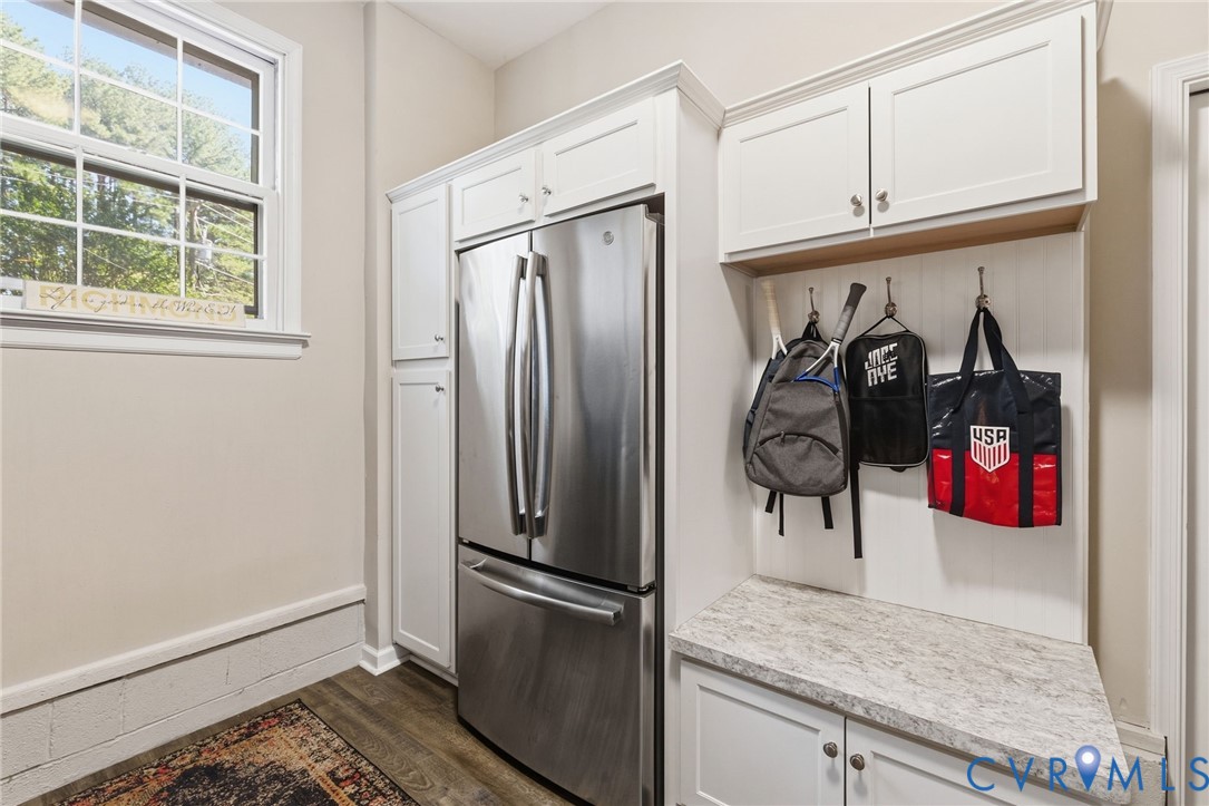 Stainless steel French door refrigerator, LVP flooring, white cabinetry with crown molding, built-in mudroom bench with textured countertop, and wall-mounted storage hooks