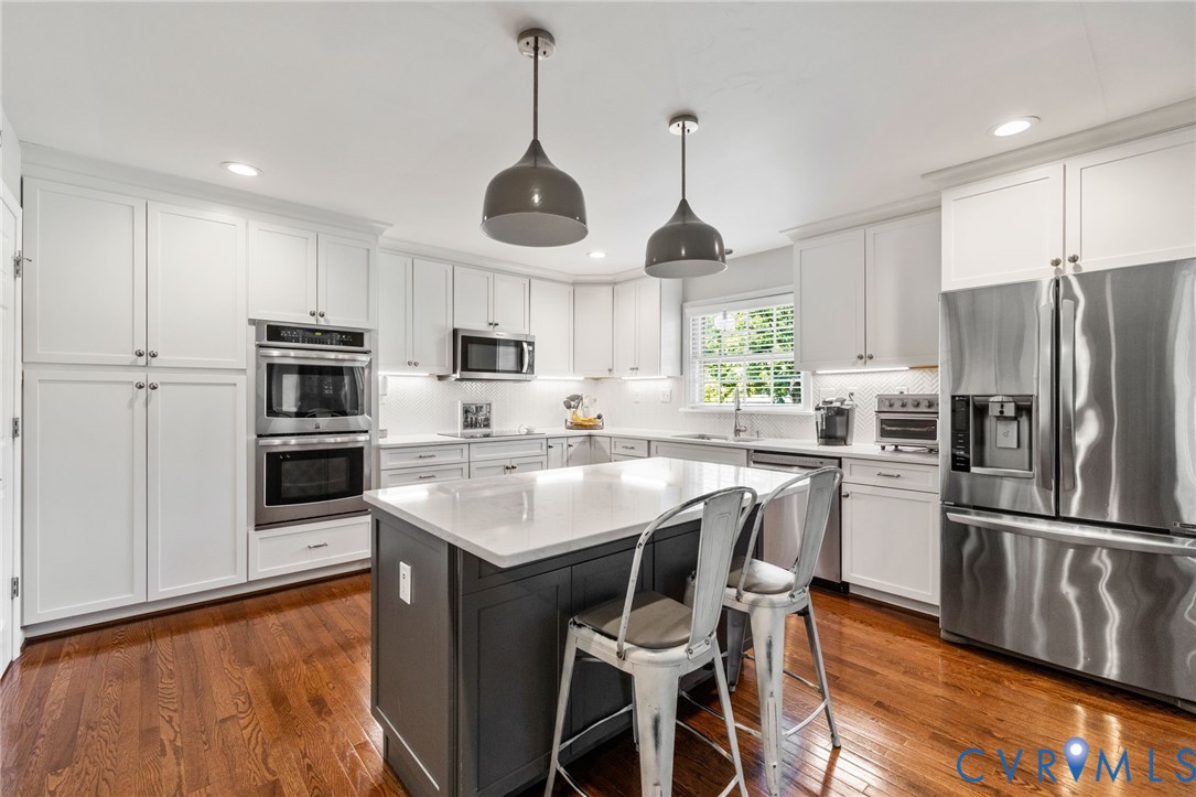 White shaker-style cabinetry, stainless steel appliances, central island with seating, hardwood floors, and recessed lighting White shaker-style cabinetry, stainless steel appliances, central island with seating, hardwood floors, and recessed lighting