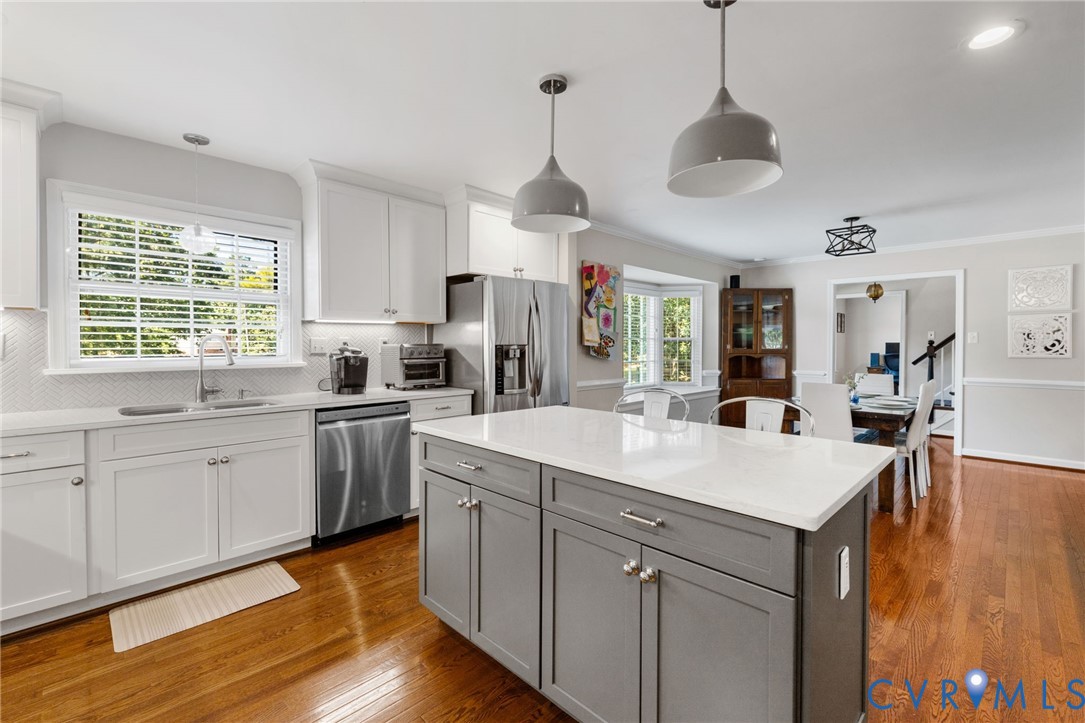 Kitchen featuring an island with quartz countertops, stainless steel appliances, pendant lighting, and hardwood flooring Kitchen featuring an island with quartz countertops, stainless steel appliances, pendant lighting, and hardwood flooring