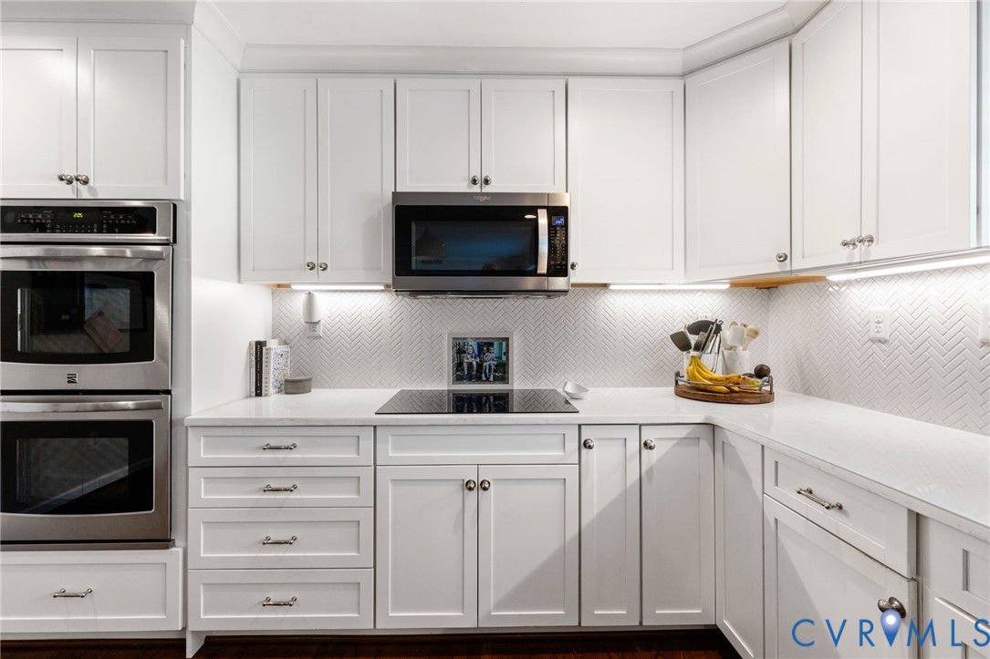 White shaker cabinetry paired with a herringbone tile backsplash, under-cabinet lighting, and a built-in double oven White shaker cabinetry paired with a herringbone tile backsplash, under-cabinet lighting, and a built-in double oven
