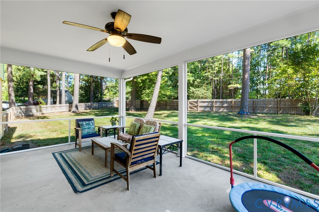 Expansive screened porch with a ceiling fan, concrete flooring, and a large fenced backyard with mature trees