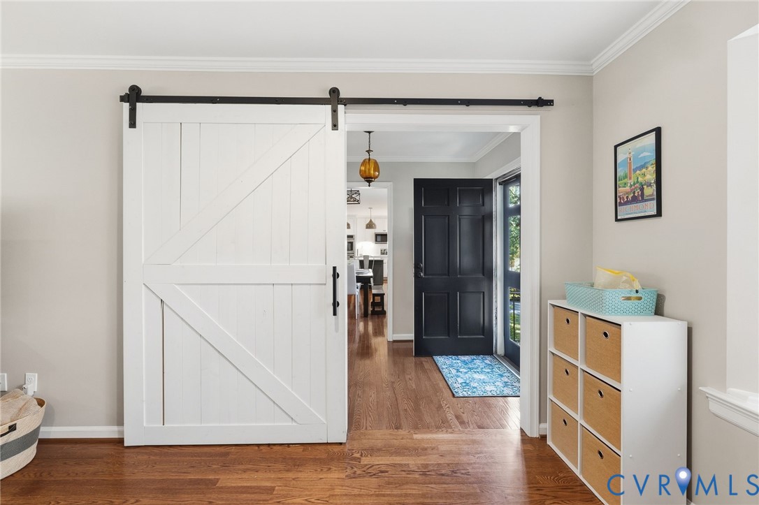 White barn door with black hardware, wood-finish flooring, crown molding, and a paneled black entry door