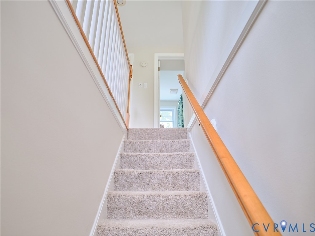 Carpeted staircase with light-toned walls, white trim, and a natural wood handrail