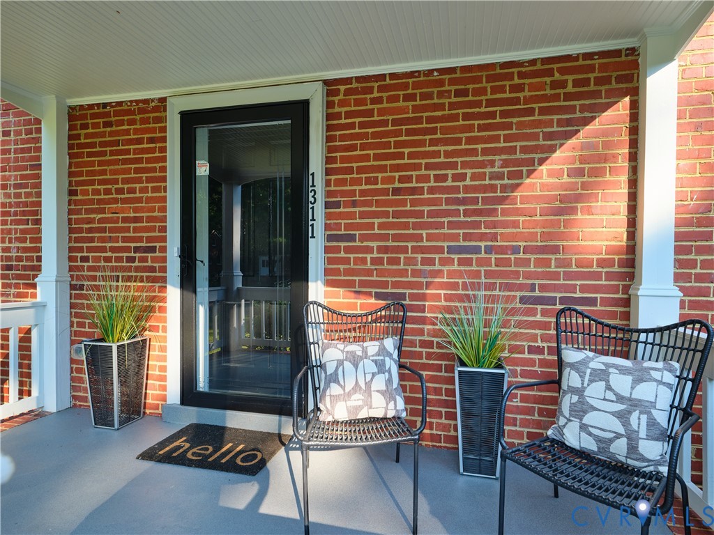 Brick exterior with a covered porch featuring beadboard ceiling, white support columns, and a black storm door