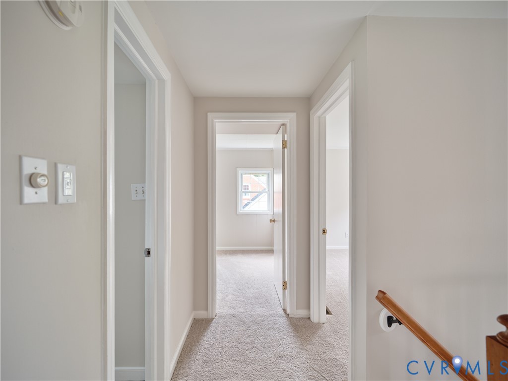 Carpeted hallway with light-toned walls, white trim, and a wood handrail