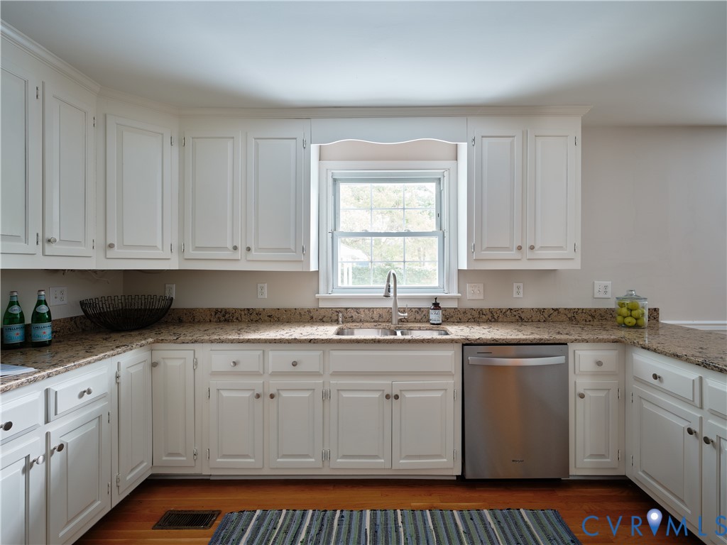 White cabinetry with crown molding, light-toned countertops, stainless steel sink with a gooseneck faucet, and a built-in stainless steel dishwasher