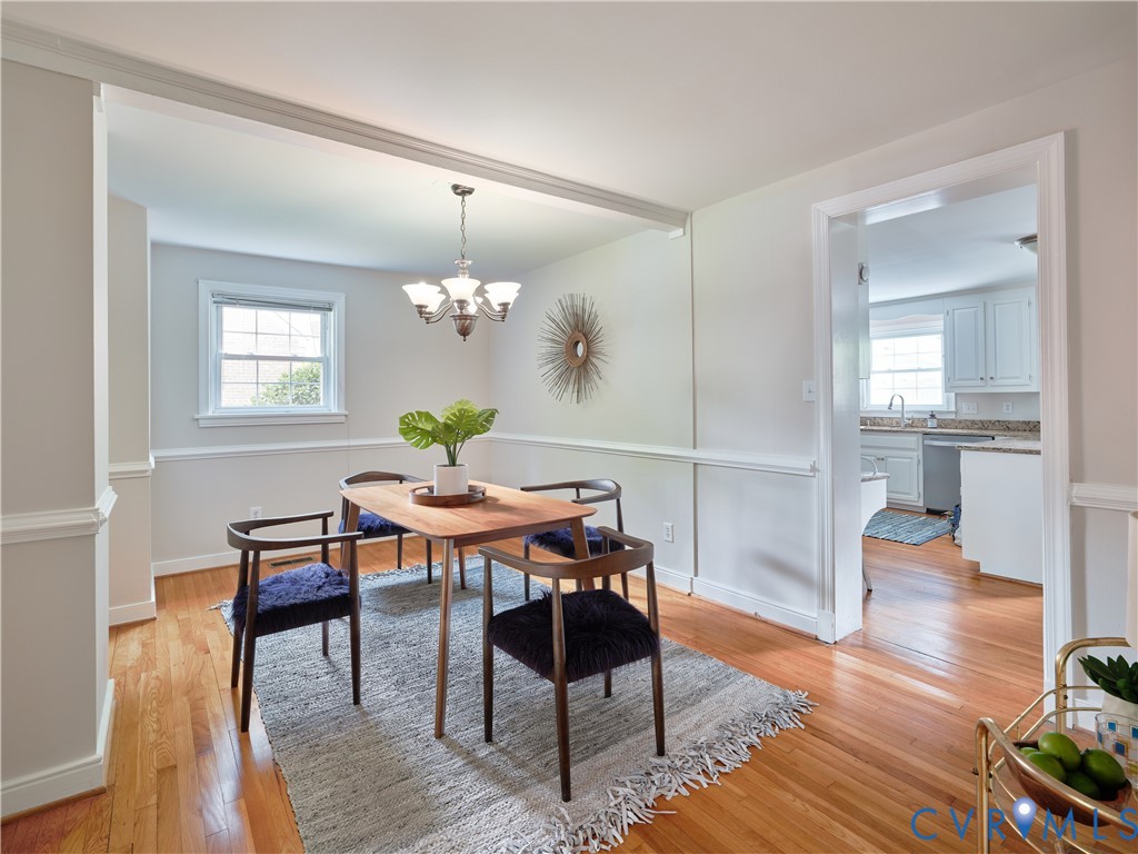 Bright, open dining area featuring hardwood flooring, wainscoting with crisp white trim, and a pendant light fixture