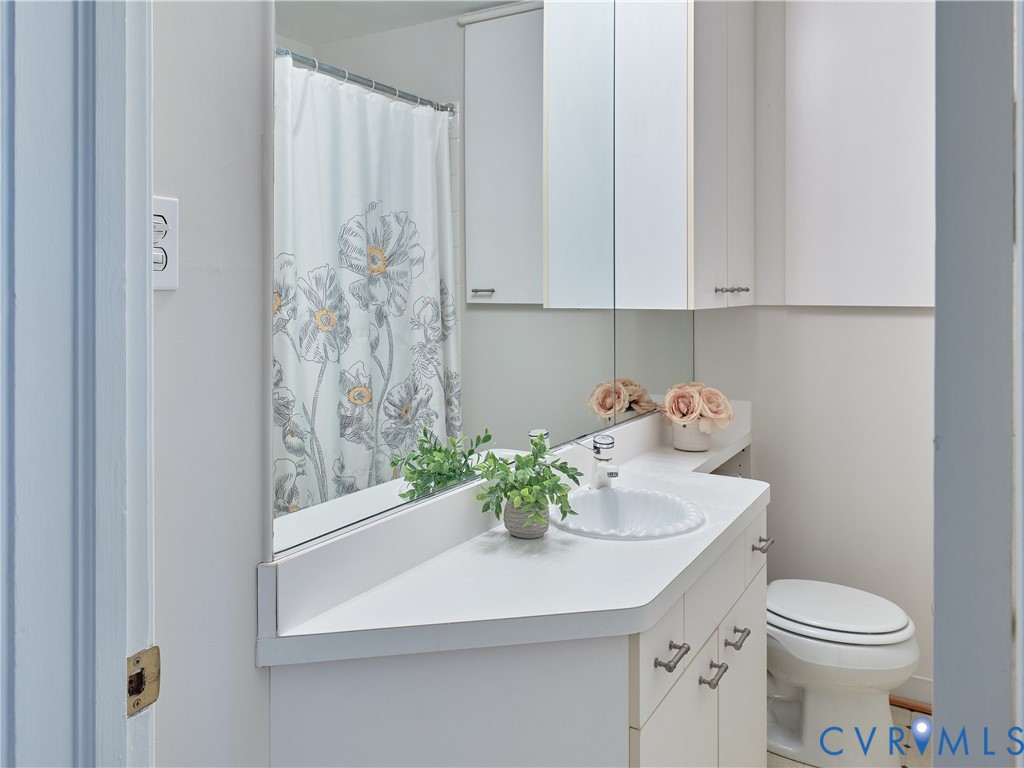 White vanity with integrated sink, white countertop, white wall-mounted storage cabinets, and a built-in toilet