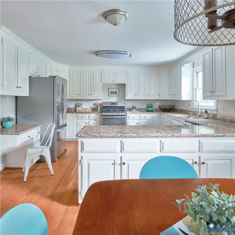 White cabinetry with dark hardware, stainless steel appliances, light-toned stone countertops, and wood-finish flooring