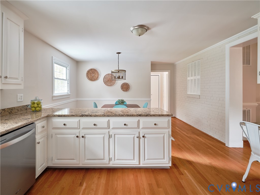 Kitchen and dining area featuring granite countertops, white cabinetry, stainless steel dishwasher, wood-finish flooring, and a decorative pendant light fixture