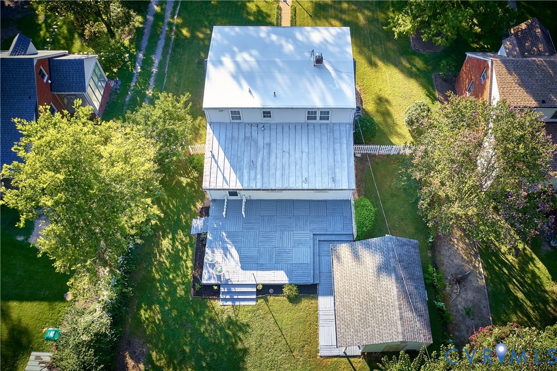 Expansive backyard featuring a large deck with patterned tile, manicured lawn, and mature trees