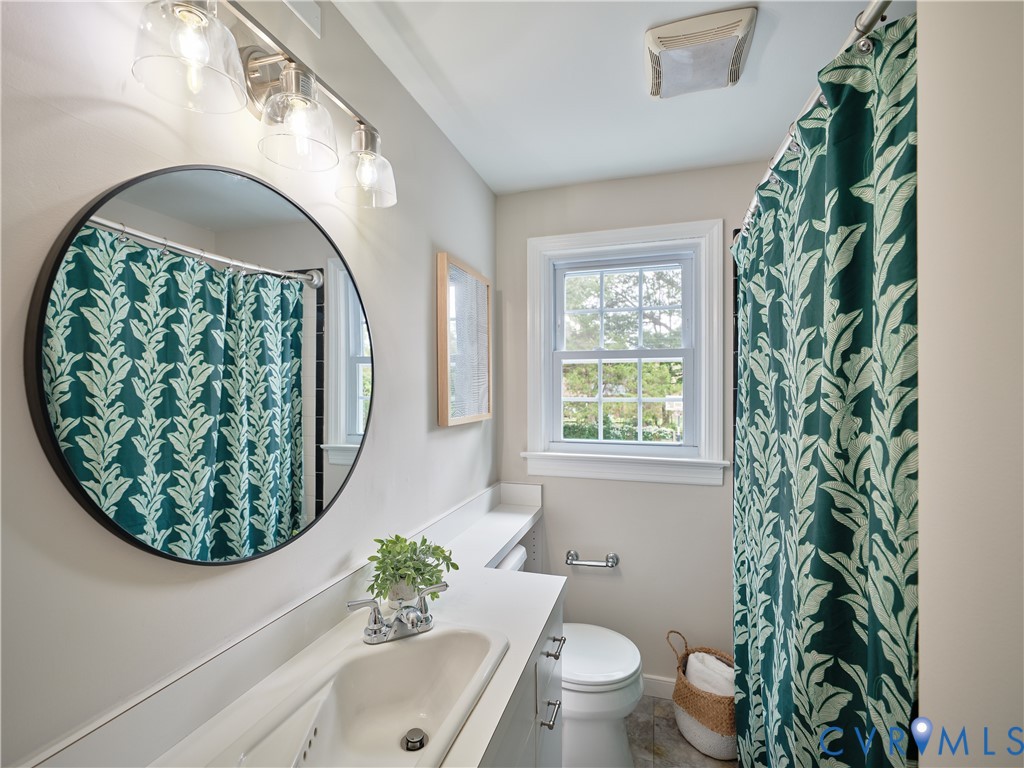 Bathroom featuring a single window, a vanity with an integrated sink, a circular mirror, and a three-light fixture