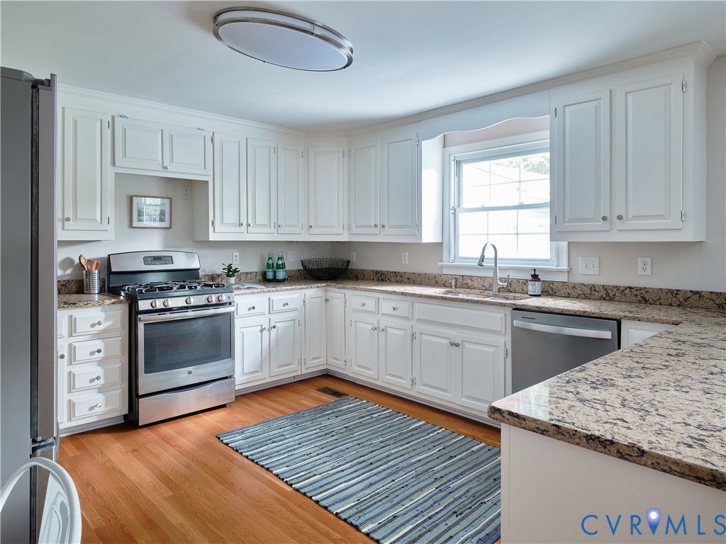 White cabinetry with crown molding, stainless steel appliances, granite countertops, hardwood flooring, and a stainless steel sink with a gooseneck faucet