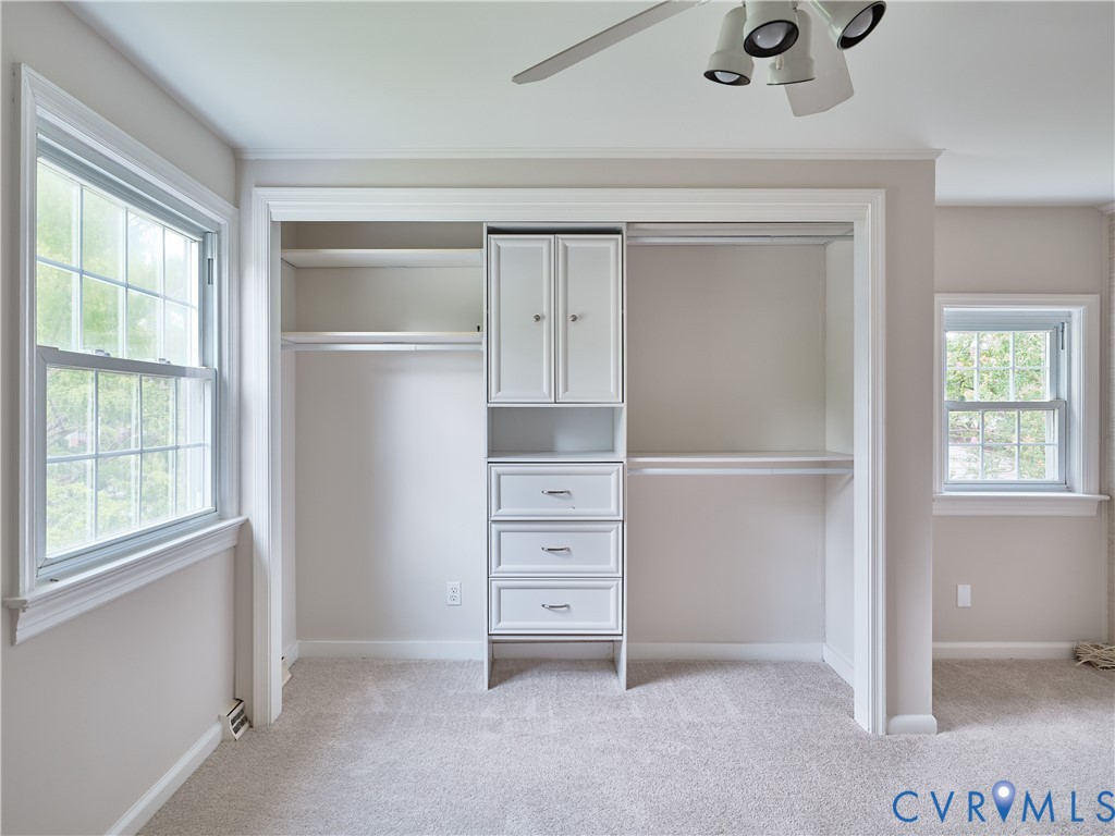 Spacious walk-in closet featuring built-in white cabinetry with dual doors, multiple shelving units, and three drawers for organized storage