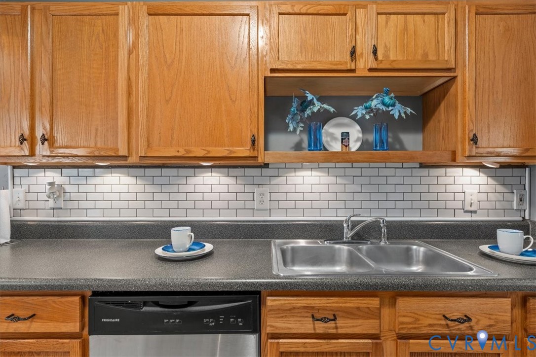 Wood cabinetry with accent shelf, subway tile backsplash, under-cabinet lighting, dual basin sink, and integrated dishwasher