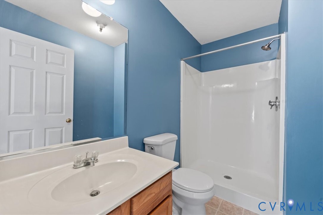 Bathroom featuring a single vanity with an integrated sink, wood-finish cabinetry, a full-width mirror, a stand-up shower, and ceramic tile flooring