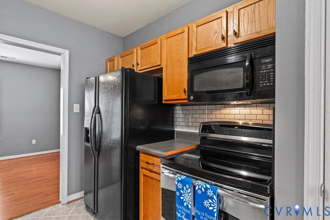 Kitchen featuring wood cabinetry, black appliances, subway tile backsplash, and light-toned flooring