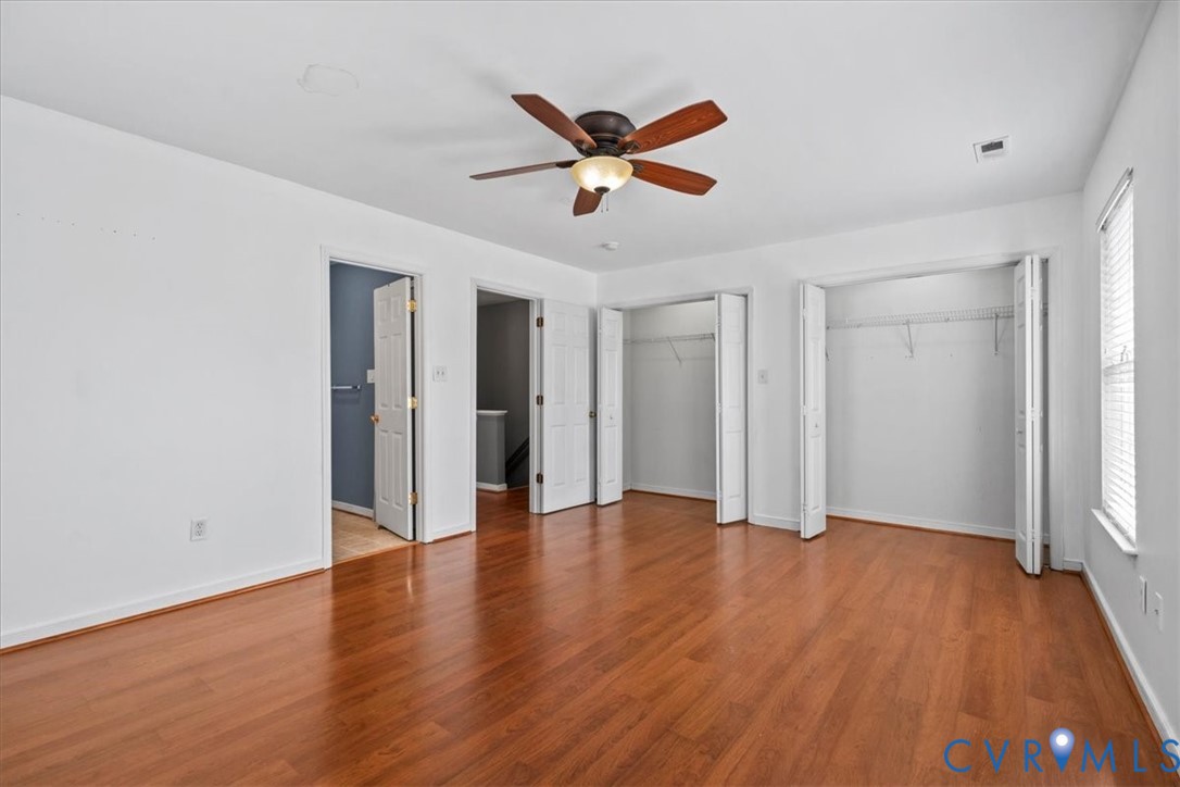 Wood-finish flooring, ceiling fan with light fixture, multiple bi-fold door closets, and white trim