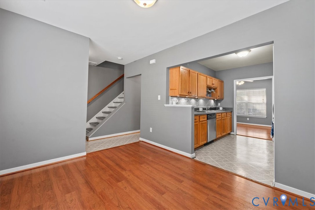 Cherry wood-finish flooring, staircase with wood handrail, kitchen featuring wood cabinetry, stainless steel dishwasher, and a gray tile backsplash