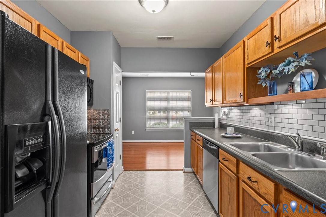 Galley kitchen featuring wood cabinetry, stainless steel appliances, a subway tile backsplash, and durable countertops