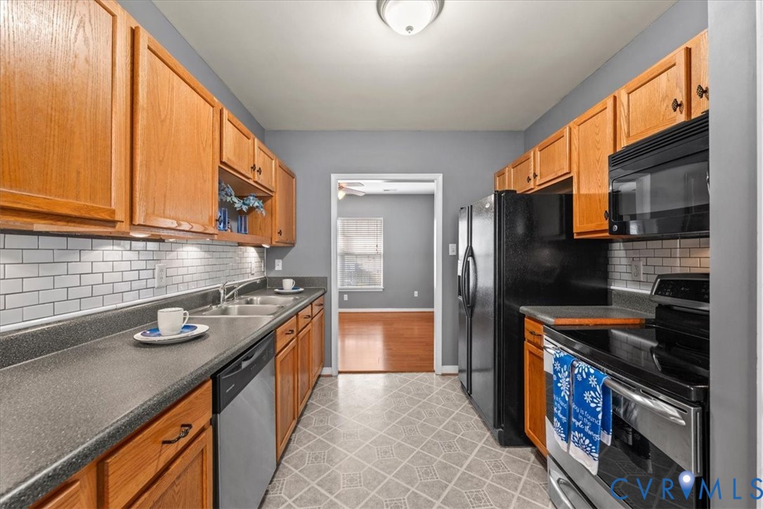 Galley kitchen featuring wood cabinetry, subway tile backsplash, dual basin stainless steel sink, and stainless steel appliances