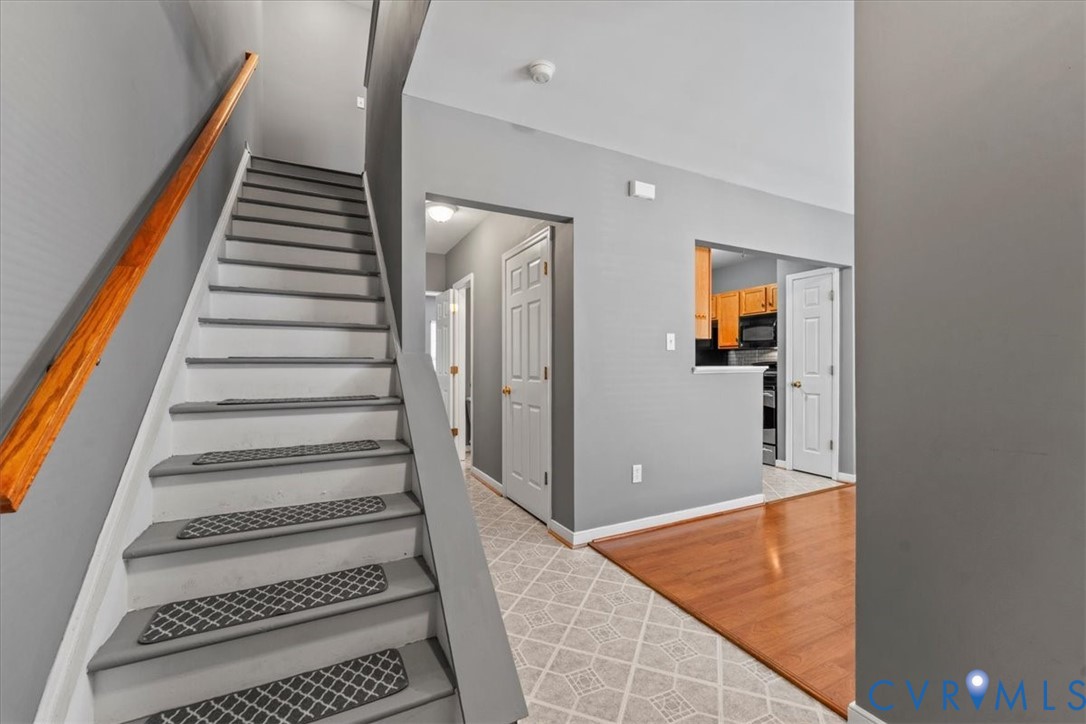 Staircase with wood handrail, light gray walls, wood-finish flooring, and patterned tile flooring