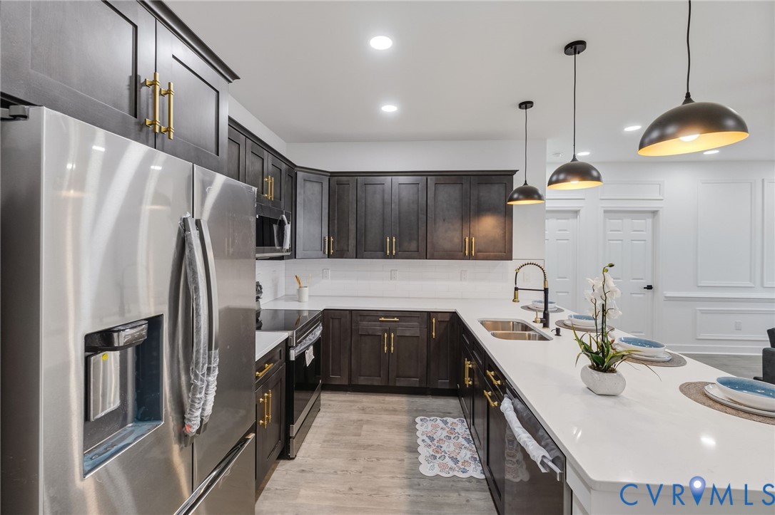 Modern kitchen featuring dark wood cabinetry, stainless steel appliances, white countertops, and pendant lighting