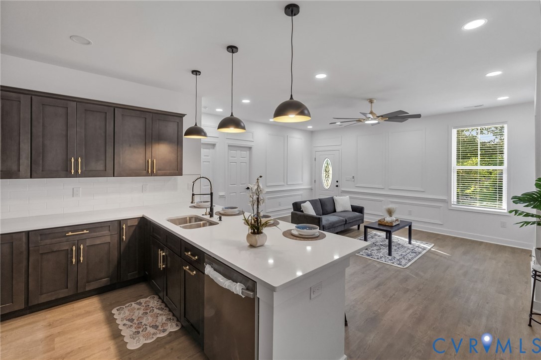 Open-concept living area featuring a kitchen island with pendant lighting, wood-finish flooring, dark wood cabinetry with gold-tone hardware, and white wall paneling