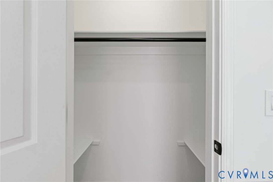 Recessed closet with a black hanging rod and white shelving